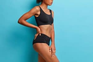 Slim woman in green workout attire has concealed tummy tuck scars.