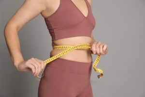Woman measuring her waist with a tape measure for weight loss.